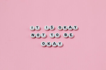 Top view of "it is okay not to be okay" quotes made out of beads on pastel background. motivation and success concept