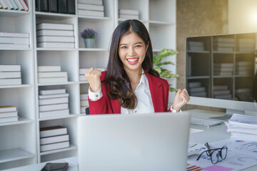 Asian business woman celebrating victory success Excited Success. Woman using laptop at work inside office holding hand up and happy triumph gesture.