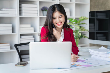 Young happy businesswoman talking on cellphone make notes and using laptop computer working online in office.