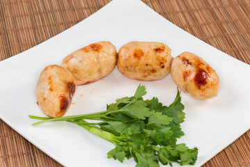 Baked thick short sausages with greens on dish, close-up