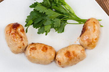 Baked thick short sausages with greens on dish, close-up