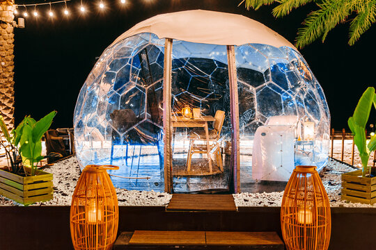 Transparent domed gazebo in the style of an igloo for romantic dates of lovers. Night view. Open air restaurant