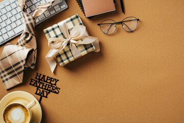 Happy Father's Day concept. Office desk table with gift box, glasses, keyboard, necktie, coffee cup on brown background.