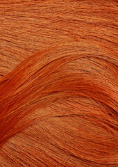 Red hair close-up as a background. Women's long orange hair. Beautifully styled wavy shiny curls. Hair coloring bright shades. Hairdressing procedures, extension.