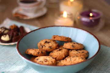 Plate of chocolate pralines, bowl of cookies, cups of tea, glasses of juice and lit candles on the table. Selective focus.