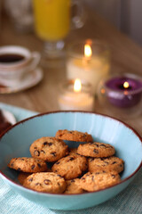 Plate of chocolate pralines, bowl of cookies, cups of tea, glasses of juice and lit candles on the table. Selective focus.