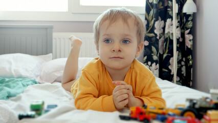 Little baby boy with dirty face playing on his bed at big window. Child development, education and entertainment