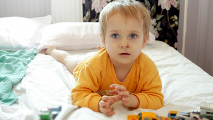 Cute funny boy with dirty face lying on bed and playing with colorful cars. Child development, education and entertainment