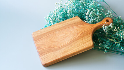 Kitchen wooden cutting board made of solid oak next to a green dried flower - gypsophila on a light pastel background. Interior of rural authentic kitchen. Natural natural lighting. Photo