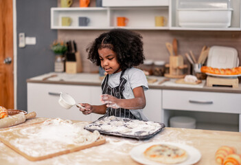 Schoolgirl prepares homemade pizza dough in funny and playful ways. Mixing ingredients like salt, sugar, milk, yeast, oil then rubbing, massaging, pressing bread flour to make it smoother, stretchier