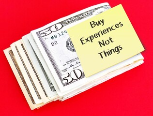 Cash dollars money on red background with note written BUY EXPERIENCES, NOT THINGS  means money can bu satisfaction from experiential purchases - travel, entertainment - than material buying