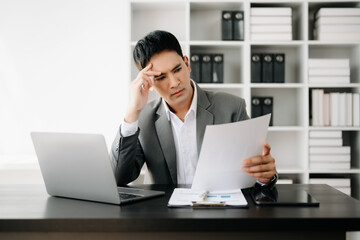 Frustrated young businessman working on a laptop computer sitting at his working place in office