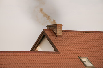 Dark smoke comes out of the chimney of a modern house in winter. Heating with solid fuel. The concept of environmental pollution