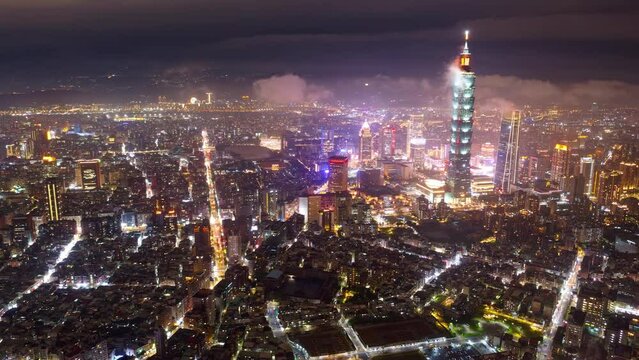 Aerial hyperlapse of Taipei, the vibrant capital of Taiwan, on a foggy evening, with 101 Tower standing out in Xinyi District, city lights dazzling in the dark and low clouds flowing among skyscrapers