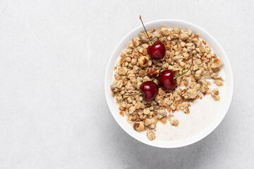 Bowl of homemade granola with nuts and cherry in white bowl on light background. Quick healthy breakfast