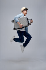 Smiling young handsome Asian tourist man with baggage jumping in mid-air ready to fly