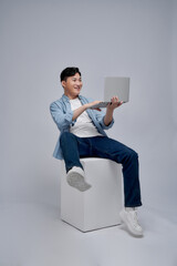 Full length photo of young excited funny guy fists up sitting platform use laptop on white background