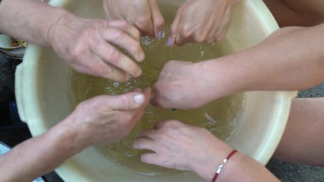 Three Women Of Different Generations Rinse Their Hands In A Basin After Washing Clothes. Family Of Elderly, Adult And Young Woman Splashing Water Raising Splashes Closeup. Slow Motion Female Hand Work