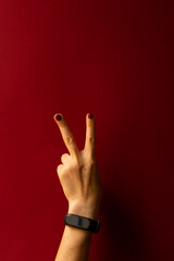 hand of a girl on a red background. Hand showing two fingers with red nails and a smart watch on the wrist. copy space	
