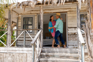 Happy caucasian senior husband and wife dancing cheerfully on balcony outside wooden cottage