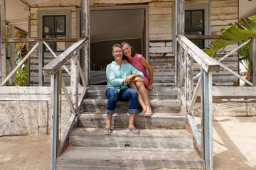 Full length of happy caucasian senior couple sitting on staircase outside wooden cottage