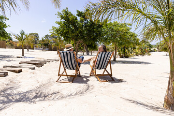 Caucasian senior couple sitting on deck chairs at beach during sunny day - Powered by Adobe