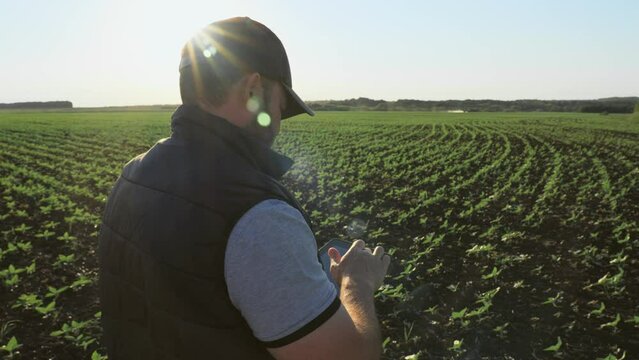 Botanist agronomist man with tablet on farm field checks inspects plants growth and collects data. Worker compiles report of plant cultivation. Caucasian male on farmland controls planting seedlings.