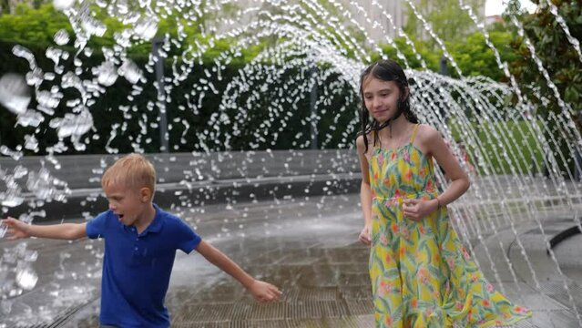 Happy children play in the park with small streams of water in the fountain. Children in wet clothes play with water in the city park, they jump and smile.