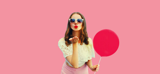 Summer portrait of beautiful young woman blowing her lips sending sweet air kiss with balloon on pink background