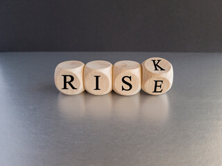 Risk vs rise symbol. Turned a wooden cube and changes the word risk to rise. Beautiful grey table, black background, copy space. Business, risk vs rise concept.