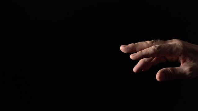 An old man's hand reaches for the light on a black background