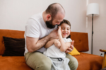 Dad tickles little son at home sofa