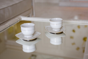 Two cups for tea on the mirror table.