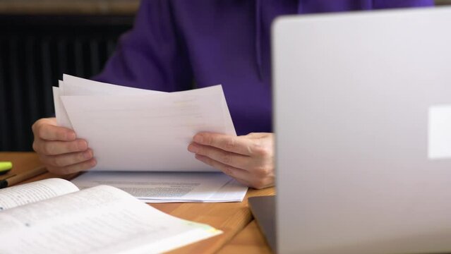 paper documents working female businessman holding papers hands looking through docs, opened laptop on table. studying, learning, reports, charts and records. concept working day education homework