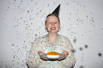 Minimal waist up portrait of smiling young woman holding Birthday cake with confetti shower at...