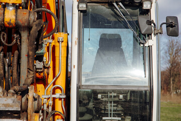 Vehicle cockpit of excavator, yellow metallic structure with transparent windshield. Operator's seat and controls ensure efficient operation on construction sites, ensuring safety and productivity