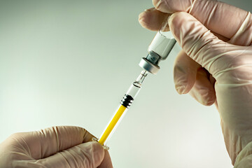 Manos con guantes soteniendo jeringa y envase de dósis de medicamento