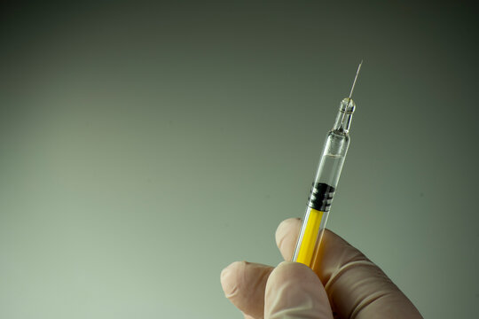 Mano con guante sosteniendo una jeringa hacia arriba.