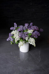 White ceramic vase purple and white flowers on a dark background.