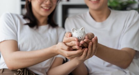 Happy asian young couple love calculate and putting coin in piggy bank for saving money to buy real...