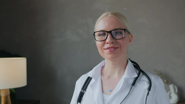 Portrait of a cute young blonde women of doctor of 35 years, which looks at the camera in the glasses and then turns toward the window. Shot with space for medical infographic. High quality 4k footage