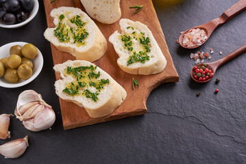 Mediterranean snacks set. Olives, oil, herbs and sliced ciabatta on a wooden board on black slate stone board over dark background, top view. Flat lay.
