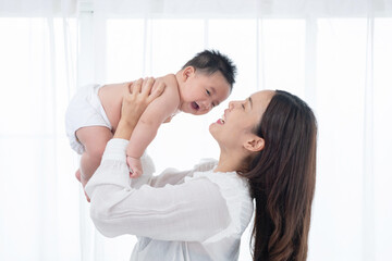 Happy family. Laughing mother lifting her adorable newborn baby son in air, copy space. asian mother lifting and playing with newborn baby, Health care family love together. Asian girl lifestyle.