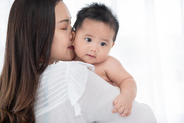 happy loving family. asian mother lifting and playing with baby in the bedroom, asia mother hug cuddle little infant or toddler, enjoy tender family moment, motherhood, childcare concept.