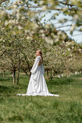 Blond blooming garden. A woman in a white dress walks through a blossoming cherry orchard. Long dress flies to the sides,