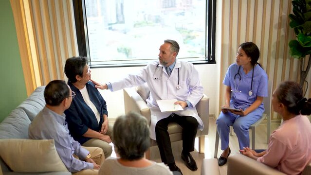 Group of happy elderly people listening to male doctors. Doctor talking to a group of elder old people in the living room in hospital. Elderly care. Medicare services.