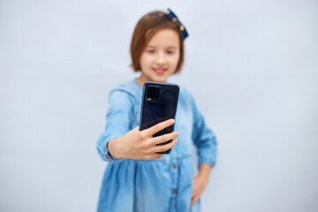 Smiling little girl in casual denim dress hold smartphone do selfie