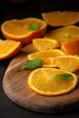 Top view of orange slices and pieces with mint leaves on wooden board, selective focus, black background, vertical