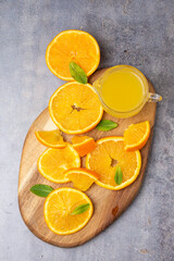 Overhead view of orange slices, pieces, mint and juice on wooden board, gray background, vertical, with copy space