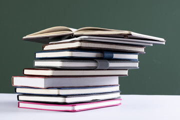Close up of stack of books and notebooks with copy space on green background